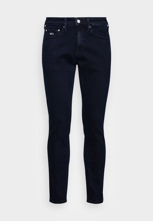 Jean slim bleu foncé avec bouton sur le devant, fermeture éclair, cinq poches et un petit patch logo sur la poche avant droite.