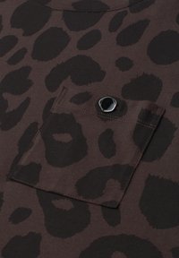 Dark brown fabric with black leopard spots pattern and a small stitched pocket secured by a single shiny black button.