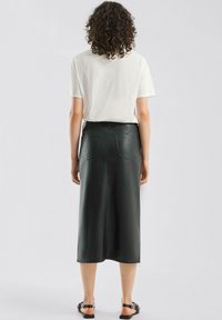 Schwarzer Leder-Midirock mit glatter Textur, Gesäßtaschen und tailliertem Bund. Kombiniert mit einem schlichten weißen T-Shirt und flachen Sandalen.