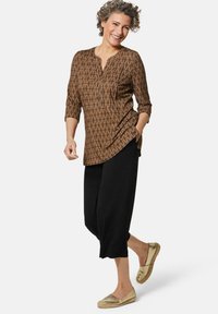 Haut à manches longues marron à motifs avec un col en V et des manches trois-quarts, associé à un pantalon noir ample et court et des chaussures dorées à enfiler.