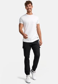 Fehér pamut póló, laza szabással. Fekete cargo nadrág oldalsó zsebekkel és rugalmas mandzsettával. Fehér sportcipők, texturált felülettel.