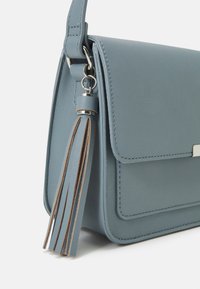 Borsa a tracolla in pelle azzurro chiaro con dettaglio a nappe appeso alla tracolla, cuciture visibili e hardware in metallo argentato su sfondo bianco.