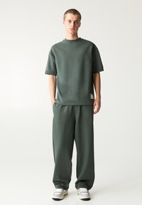 Zöld pamut keverék oversized póló és hozzáillő, magas derekú nadrág. Puha tapintás, laza szabás és minimalista dizájn diszkrét márkázással.