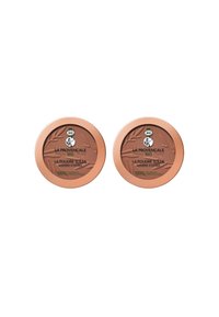 Deux compacts ronds de bronzer avec une poudre brun clair. Chacun a un couvercle de couleur bronze avec des détails de logo verts et noirs.