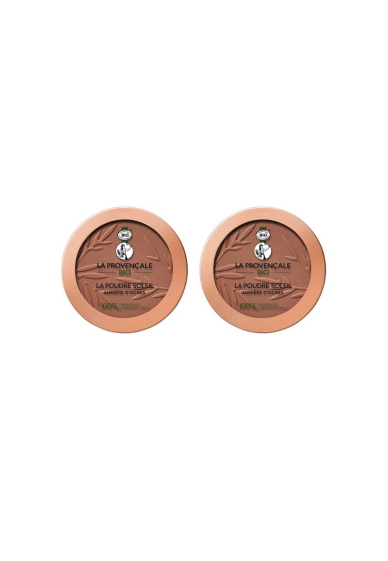 Deux compacts ronds de bronzer avec une poudre brun clair. Chacun a un couvercle de couleur bronze avec des détails de logo verts et noirs.