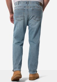 Vaqueros de mezclilla azul claro con corte recto, que presentan dos bolsillos traseros y una cinturilla cosida, combinados con botas de trabajo de color marrón claro.