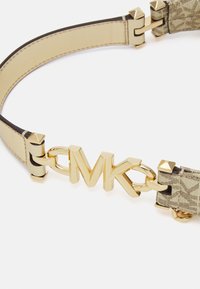 Beżowy skórzany pasek z bukletem MK w odcieniu złota, z ćwiekami i wzorzystą tkaniną. Gładka tekstura z metalowymi detalami.