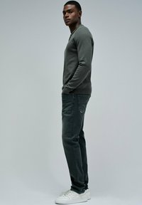 Šedý svetr s dlouhým rukávem, kombinovaný s tmavými džínami a bílými teniskami. Svetr má kulatý výstřih; džíny obsahují boční kapsy a mají vybledlou texturu.
