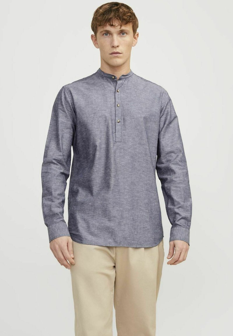 Camicia a maniche lunghe da uomo in tessuto chambray azzurro chiaro. Caratterizzata da un colletto a banda stretto e una placca con tre bottoni. Texture liscia e vestibilità regolare.