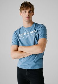 Lyseblå bomulds T-shirt med "Red Bull Racing" grafik i hvid, korte ærmer, rund hals og en afslappet pasform. Mørke jeans fuldender looket.