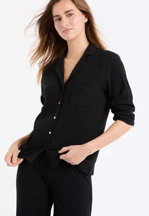 Conjunto de pijama negro con textura de canalé que incluye una camisa abotonada con cuello y un bolsillo en el pecho. La tela parece suave y tiene un patrón texturizado.