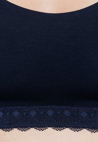 Top in blu navy realizzato in un tessuto liscio e elasticizzato, con un delicato bordo in pizzo lungo il fondo. Presenta un design con scollatura arrotondata.