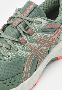 Zielono-koralowe buty do biegania Asics z wzorzystymi sznurówkami, teksturowanym siateczkowym wierzchem i amortyzującą podeszwą.