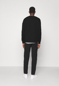 Černá mikina s ribovanými manžetami a kulatým výstřihem, doplněná o černé tepláky se bočními pruhy. Bílá obuv dokončuje vzhled.