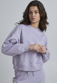 Felpa lilla con collo a giro, vestibilità rilassata e maniche a sbuffo. Tessuto morbido, polsini e orlo a costine, abbinata a pantaloni coordinati.