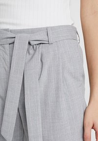 Světlé šedé kalhoty s proužkováním a zavazovacími pasek, vyrobené z texturední tkaniny a s bočními kapsami. Jednoduchý a moderní střih.