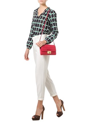 Woman wearing patterned black and white blouse, white rolled-up pants, brown high heels, and carrying a red quilted shoulder bag.