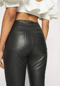 Svarta läderbyxor med smal passform, som har två bakfickor och synlig sömnad. Slät struktur och hög midja.