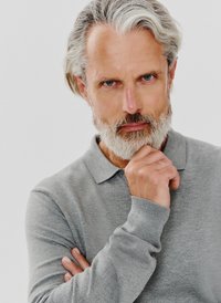 Szara koszulka polo o subtelnym wzorze, z kołnierzykiem. Model ma pełną brodę i jest ustawiony w zamyślonej pozycji.