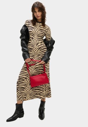 Robe à rayures zébrées en beige et noir, associée à une veste en cuir noir, un sac à main tissé rouge et des bottines noires à clous.