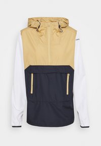 Bundy proti větru s kapucí v béžové barvě na vrchu, námořnicky modrá přední kapsa a bílé dlouhé rukávy, s půlzipem a nastavitelnými šňůrkami kapuce.