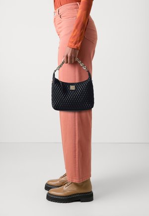 Černá prošívaná kabelka s opleteným řetězovým uchem, se zlatou logovou destičkou. V kombinaci se světle růžovými širokými kalhotami a béžovými šněrovacími botami.