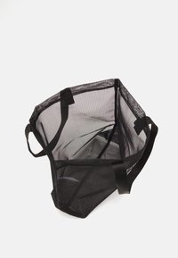 Sac fourre-tout en maille noire avec ouverture sur le dessus, tissu robuste, deux poignées, de forme carrée et design transparent.