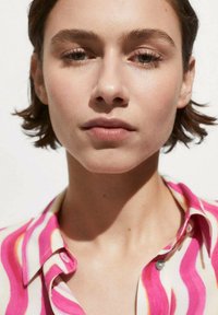 Close-up of a person with short hair wearing a pink and white striped shirt. The shirt features wavy patterns and a buttoned collar.
