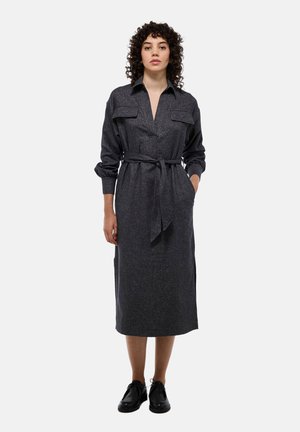 Robe chemise longue à manches longues grise foncée avec un col, deux poches poitrine, une ceinture en tissu, des fentes latérales et un motif texturé. Associée à des chaussures noires.