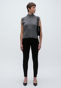 Pulover gri fără mâneci cu guler înalt și tiv striat, asortat cu pantaloni negri mulați și tocuri negre cu vârf ascuțit. Design minimalist, siluetă elegantă.