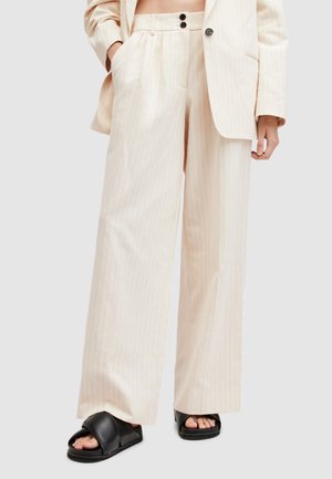 Beige gestreepte broeken met een ontspannen pasvorm, met een hoge taille, twee voorzakken en een op maat gemaakte uitstraling. Gecombineerd met zwarte instapsandalen.