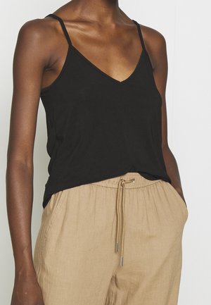 Schwarzes V-Ausschnitt-Camisole mit dünnen Trägern, aus weichem Stoff; getragen mit beigen, leichten Hosentaschen mit Kordelzug und entspannter Passform.