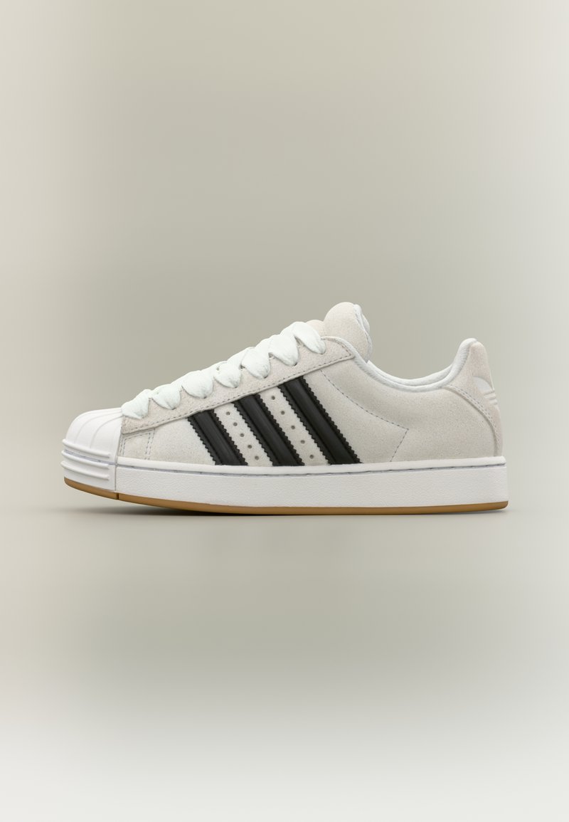 Witte suède sneakers met drie zwarte strepen, een rubberen neuskap en witte veters. Voorzien van een rubberen buitenzool in gumkleur en een afgeronde hiel.