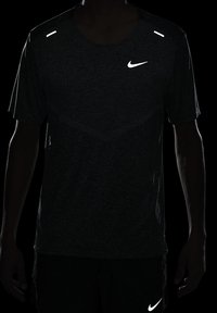 Camisa deportiva de manga corta de Nike en gris oscuro, con acentos reflectantes en los hombros y el logo. Tejido ligero que absorbe la humedad.