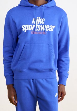 Felpa blu Nike con logo e testo bianco, materiale misto cotone, tasca a scomparsa frontale, polsini e orlo a costine, vestibilità rilassata.