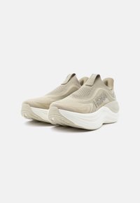 Ζευγάρι μπεζ αθλητικά παπούτσια χωρίς κορδόνια με πλεκτό επάνω μέρος, χοντρή λευκή κυματιστή σόλα και λογότυπο "HOKA" στο πλάι, που εμφανίζονται σε λευκό φόντο.