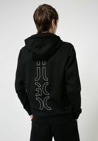 Felpa nera con finitura testurizzata, caratterizzata da un grande logo bianco sul retro. Progettata con cappuccio e polsini a costine.