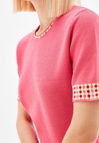 Rosa stickad topp med rund halsringning, med färgglada mönstrade detaljer på ärmarna. Texturen verkar mjuk och lätt.