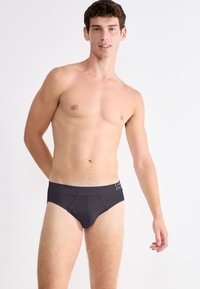 Schwarze Badehose mit enganliegendem Schnitt, elastischem Bund und dezentem Logo. Die Materialien wirken glatt und dehnbar mit minimaler Gestaltung.