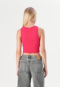 Tilpasset, ribbestrikket croptop i rosa med rund hals. Kombinert med høyhalsede grå denimjeans med merkepute og baklommer.