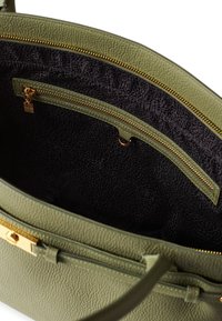 Grüner strukturierter Innenraum einer Handtasche mit schwarzem Stofffutter. Enthält eine Reißverschlusstasche und goldfarbene Hardware-Akzente.