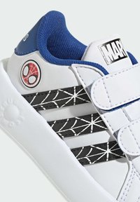 White sneaker with blue accents, featuring a Spider-Man logo, black striped panels with a web pattern, and a hook-and-loop strap for closure.