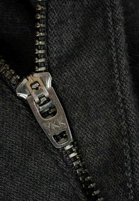 Black fabric with a silver YKK zipper. The zipper has a metallic pull tab and visible teeth along its length, showcasing durable stitching.