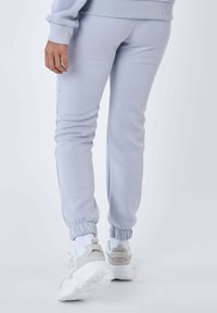 Lichtgrijze joggingsbroek met een slim fit, elastische boorden en een zachte textuur, gecombineerd met witte en grijze sneakers.