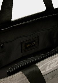Borsa tote grigia e nera aperta che mostra una tasca interna con zip e un'etichetta in tessuto nero con il logo dorato "LIU JO" e un bordo decorativo.