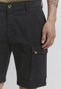 Zwarte cargoshorts van stevig materiaal hebben een zijzak met knoopsluiting en een zichtbare taillebandknop.