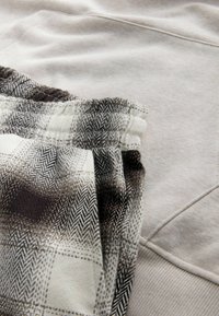 Lys grå sweatshirtstof parret med mønstrede joggers med et hundetandsdesign i sort, hvidt og gråtoner.