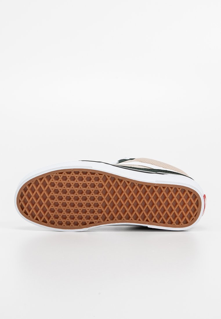 Chaussure avec une semelle en caoutchouc brun texturé arborant un motif alvéolaire, une semelle intermédiaire blanche et des accents noirs sur un dessus beige.