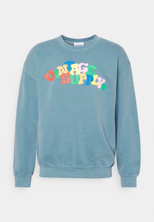 Sweat-shirt bleu à col ras du cou avec texte "Vintage Supply" multicolore et incurvé sur la poitrine, et poignets et ourlet côtelés.