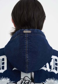 Dunkelblauer Denim-Hoodie mit einer genähten Kapuze und dekorativen weißen Grafiken auf dem Rücken, einschließlich floraler Muster.